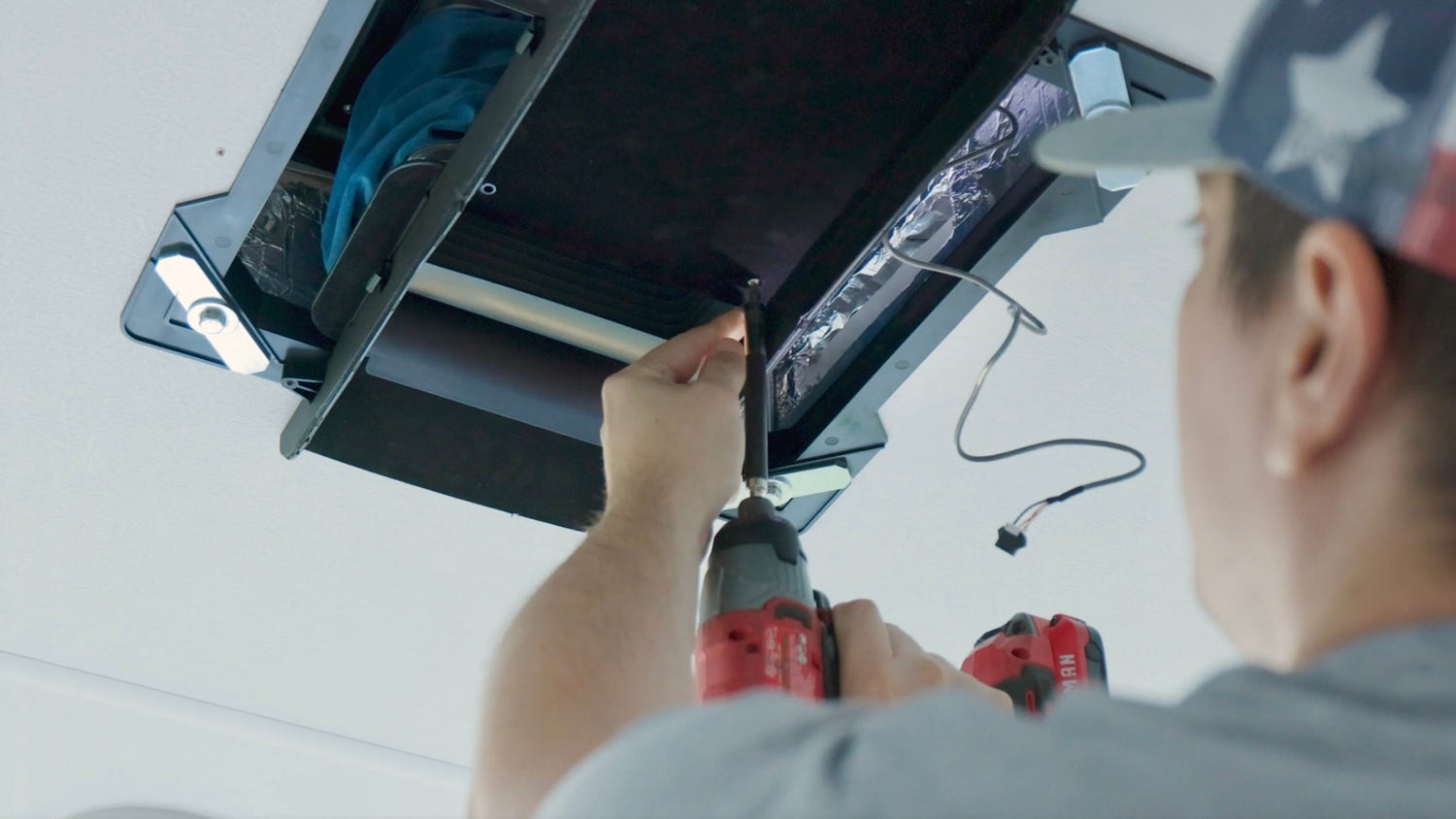 Person lookin up at the RV ceiling and screwing in a part on the new AC unit he is installing.
