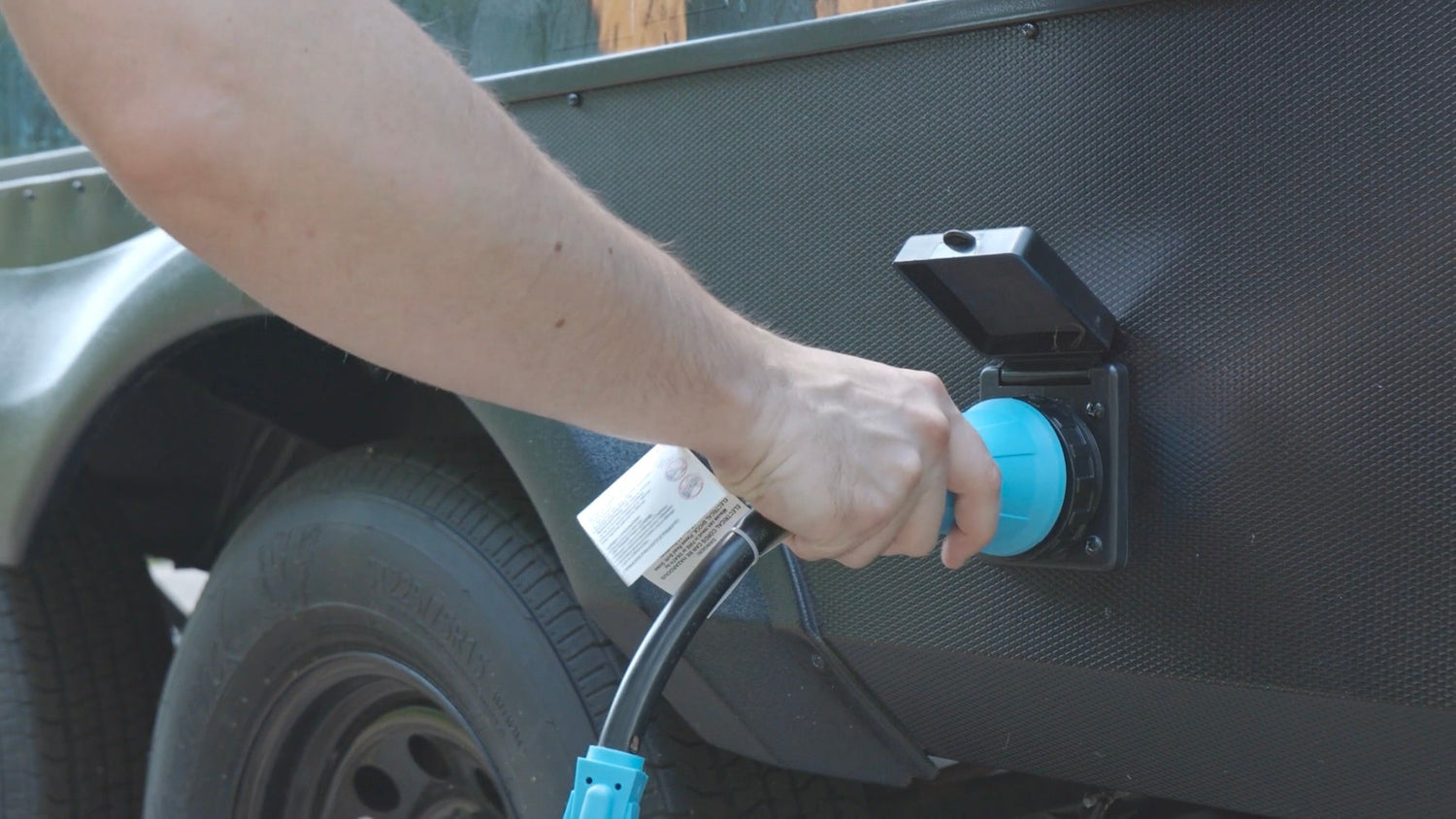 A person's hand is pulling the plug on the outside of the RV to disconnect power.