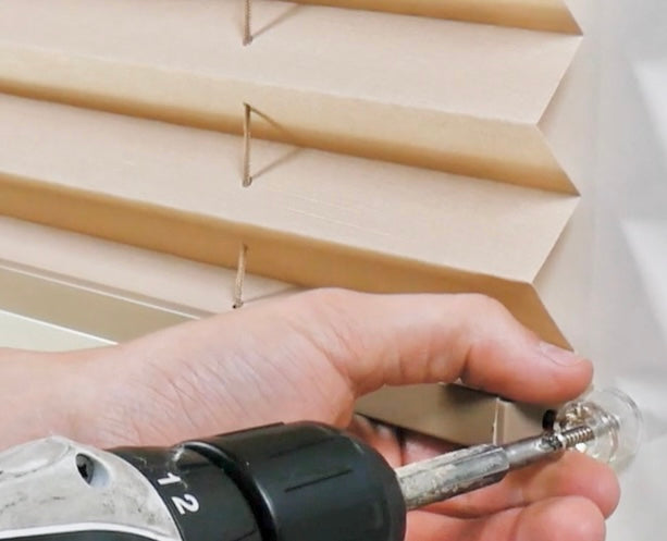 A person holding a drill and screwing in a screw to install pleated shades in an RV.