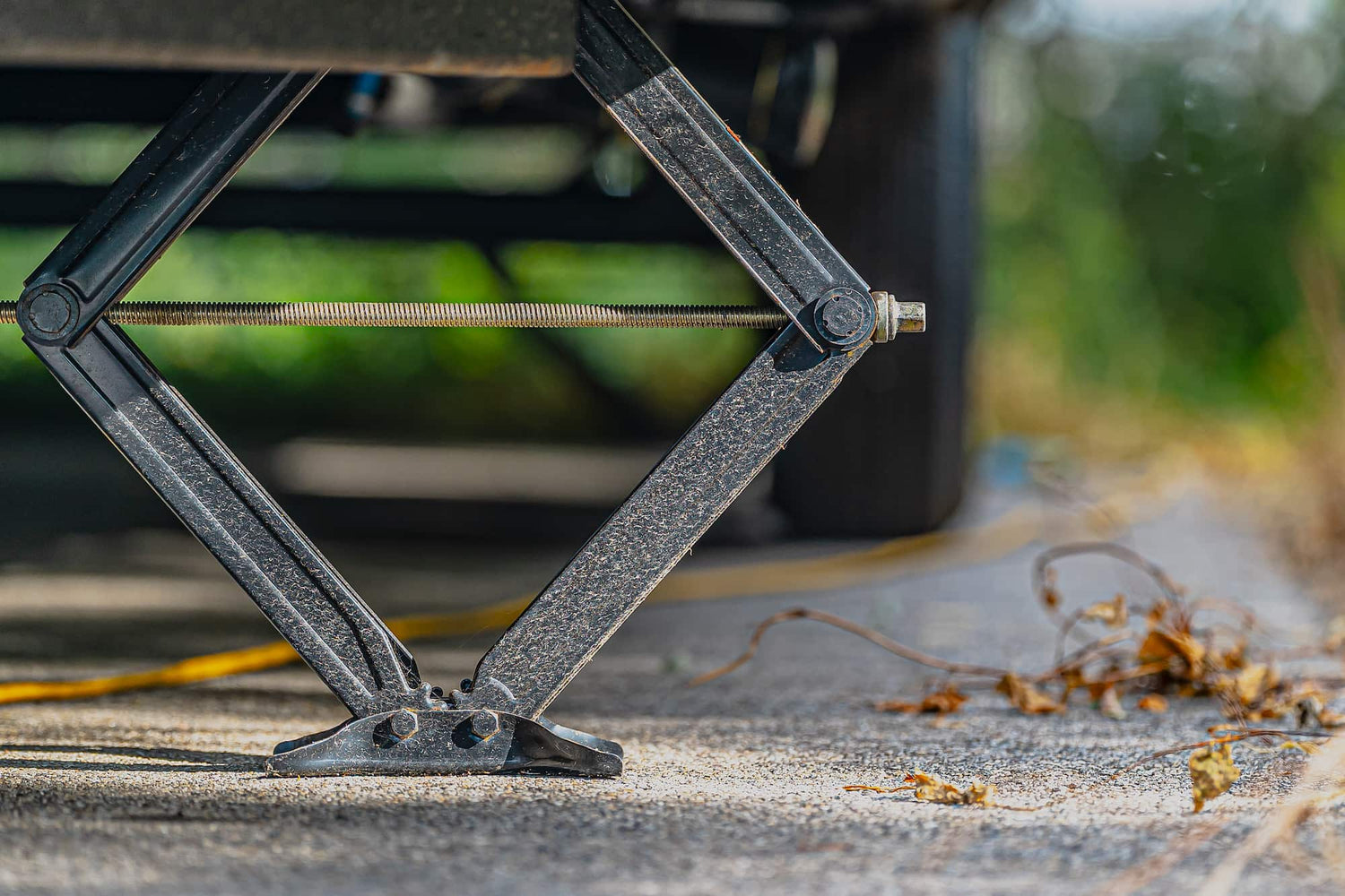 A scissor jack under a toy hauler, outside with leaves on the ground.
