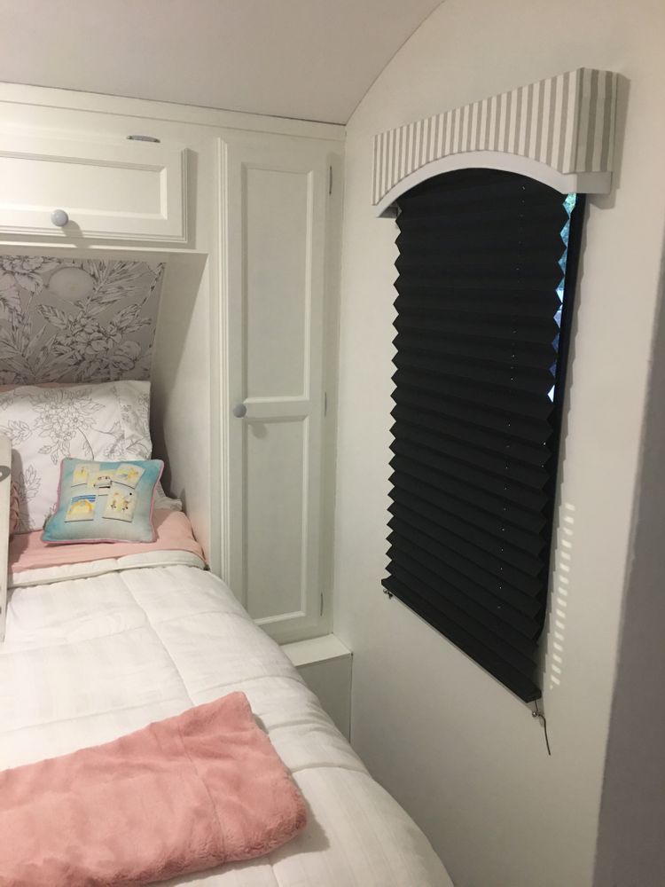 RV bedroom with a bed and black pleated shades covering the window.