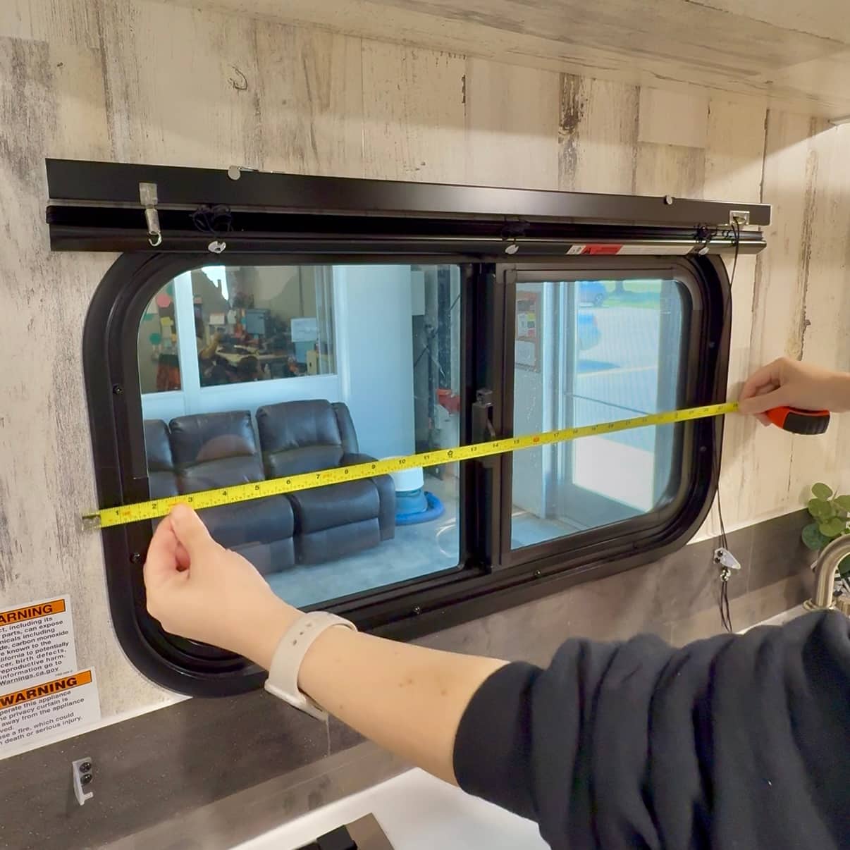 A person holds up a measuring tape to an RV window, to measure for new shades.